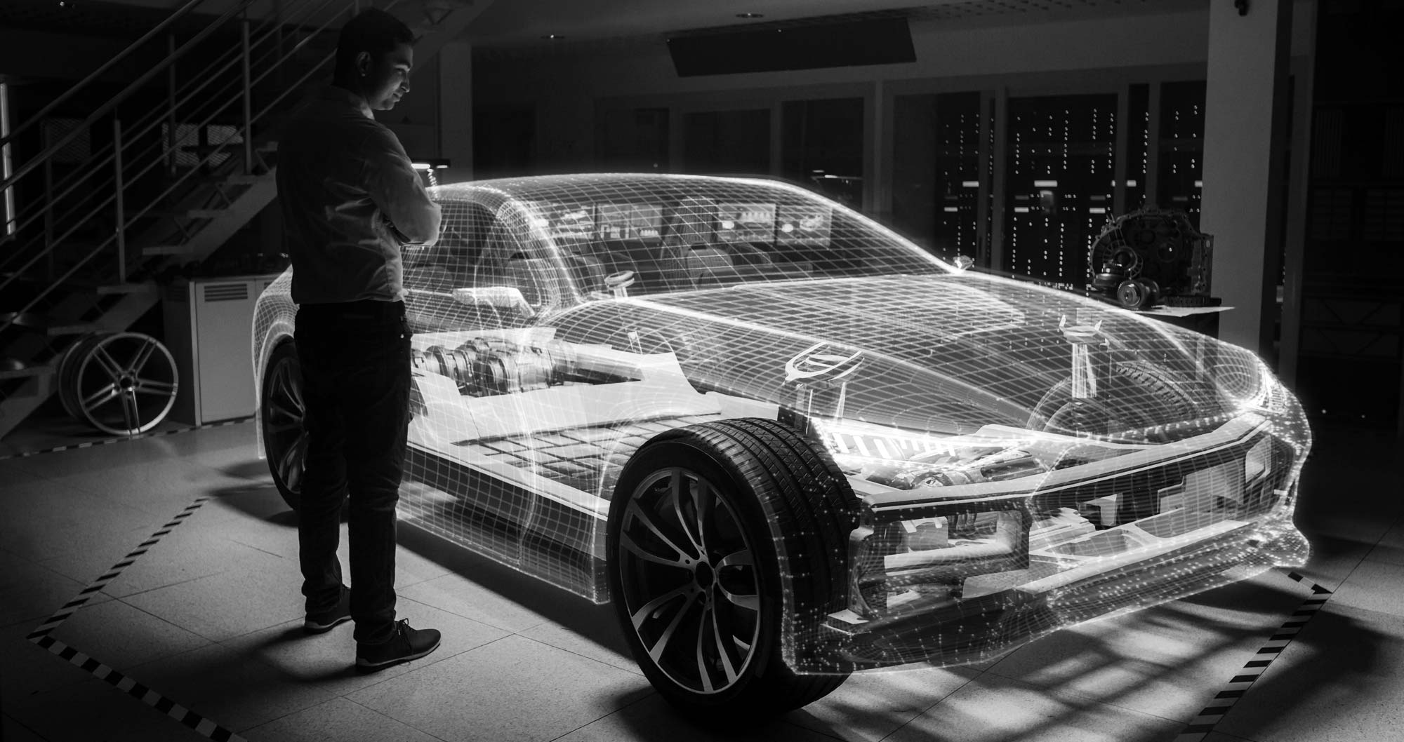Uomo in piedi all'interno di una officina che ammira autovettura con carrozzeria wireframe semitrasparente che mostra le parti meccaniche.
